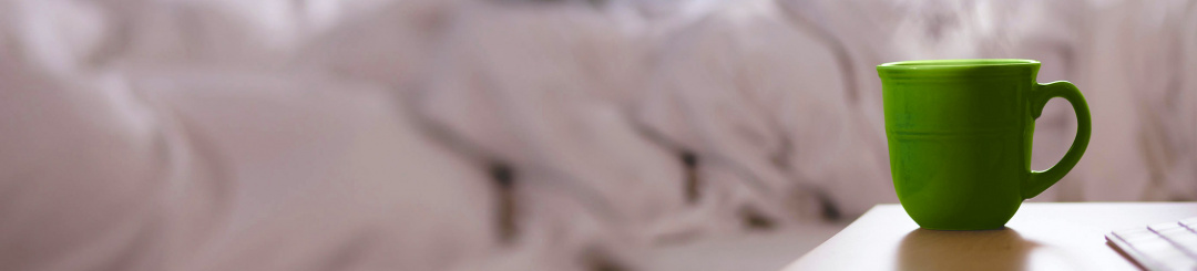 Green mug in front of a bed